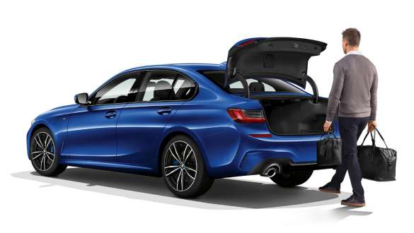BMW 3 серии Седан (G20), функция автоматического открывания крышки багажного отделения. Вид в три четверти на седан BMW 3 серии (G20), водитель автоматически открывает заднюю дверь с помощью ноги.
