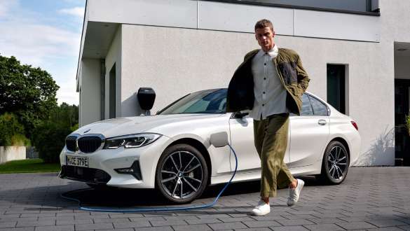 Плагин-гибрид BMW 3 серии Седан 2021 G20, вид спереди в три четверти, подключен к зарядке Плагин-гибрид BMW 3 серии Седан 2021 G20, вид спереди в три четверти, подключен к зарядке с моделью