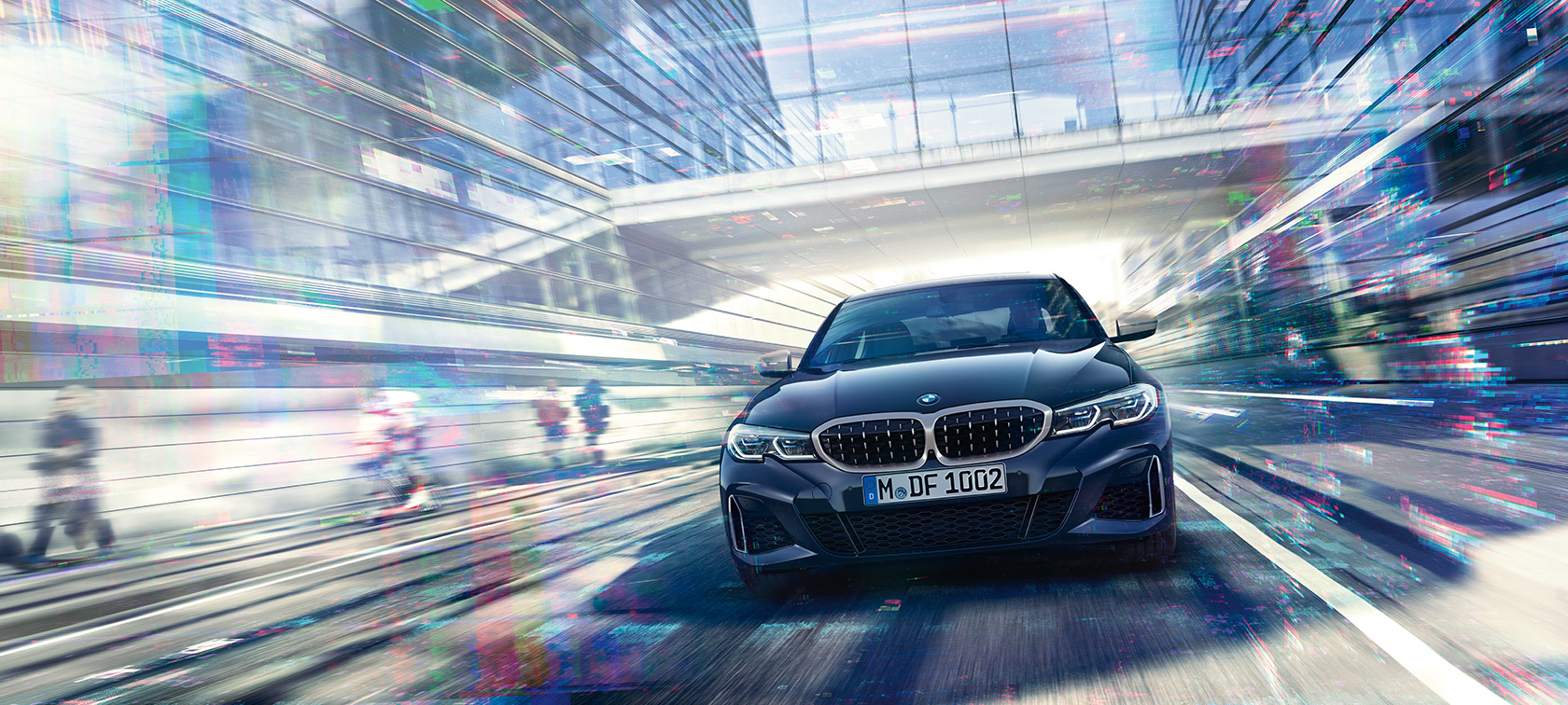 BMW 3 серии Седан, вид спереди BMW M340i xDrive. Вид спереди седана BMW M340i xDrive в движении между городскими стеклянными постройками.
