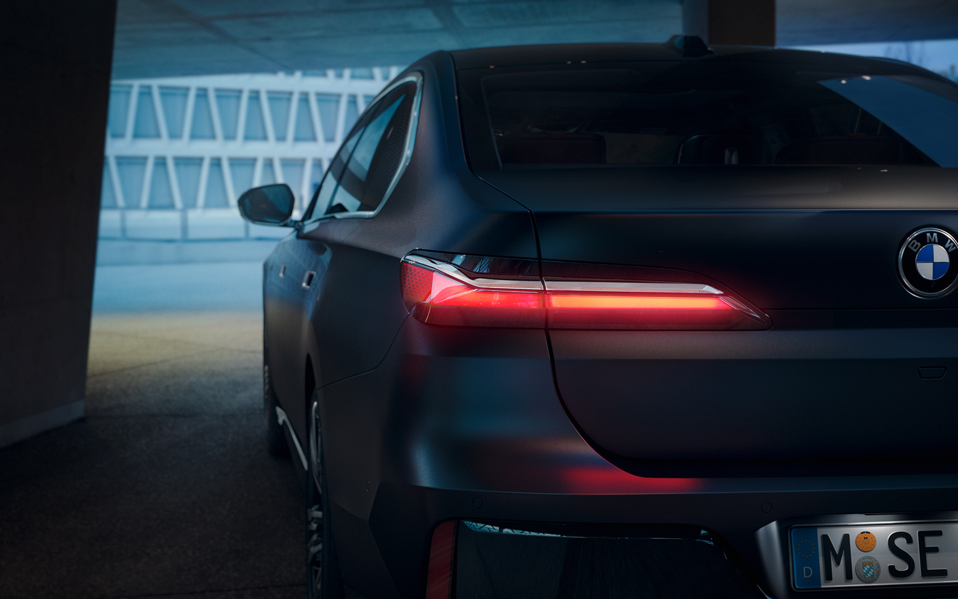 BMW 7 Серии Седан G70 ICE740i пакет M Sports, окраска кузова серый металлик (Frozen Deep Grey), вид сзади BMW 7 Series Sedan G70 ICE 740i M sports package Frozen Deep Grey metallic rear view with red glowing taillight in tunnel