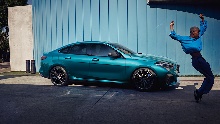 BMW M235i xDrive Gran Coupe F44, вид сбоку с женщиной перед автомобилем BMW M235i xDrive Gran Coupe F44, "Синий Снэппер Рокс металлик", вид сбоку с женщиной перед автомобилем