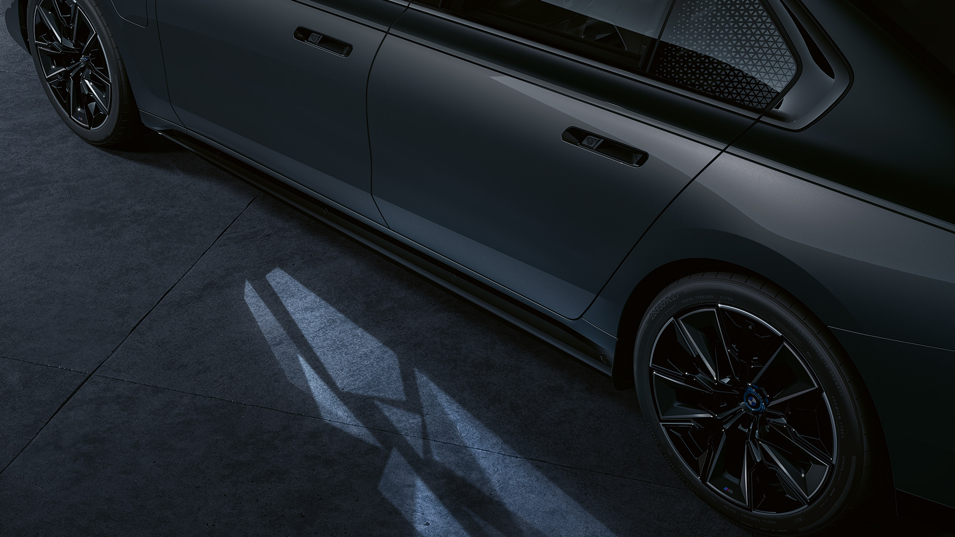 Концепция освещения BMW M760e xDrive G70 Концепция освещения BMW M760e xDrive G70, двухцветная окраска кузова BMW Individual (черный металлик Black Sapphire и серый металлик Dravite Grey), вид сбоку с активированной функцией Welcome Light Carpet, крупный план