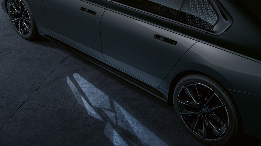 Концепция освещения BMW M760e xDrive G70, двухцветная окраска кузова BMW Individual (черный металлик Black Sapphire и серый металлик Dravite Grey), вид сбоку с активированной функцией Welcome Light Carpet, крупный план