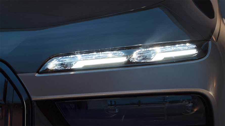 Включенные фары головного света BMW Crystal Iconic Glow на BMW M760e xDrive G70 крупным планом, двухцветная окраска кузова BMW Individual (черный металлик Black Sapphire и серый металлик Dravite Grey)