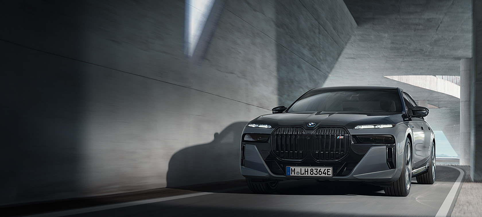 BMW M760e xDrive G70 с пакетом M Performance едет по улице, двухцветная окраска кузова BMW Individual (черный металлик Black Sapphire и серый металлик Dravite Grey), вид спереди в 3/4