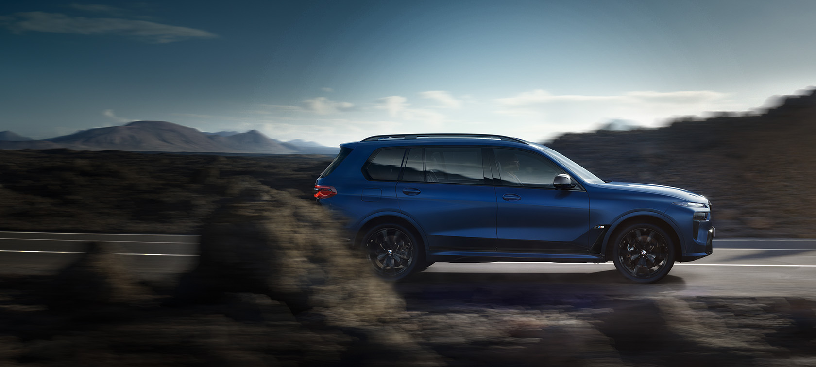 BWM X7 M60i G07 LCI көк Frozen Marina Bay Blue түсті, көшеде қозғалыста, жанынан көрінісі BWM X7 M60i G07 LCI көк Frozen Marina Bay Blue түсті, тау пейзажының фонында далада, жанынан көрінісі