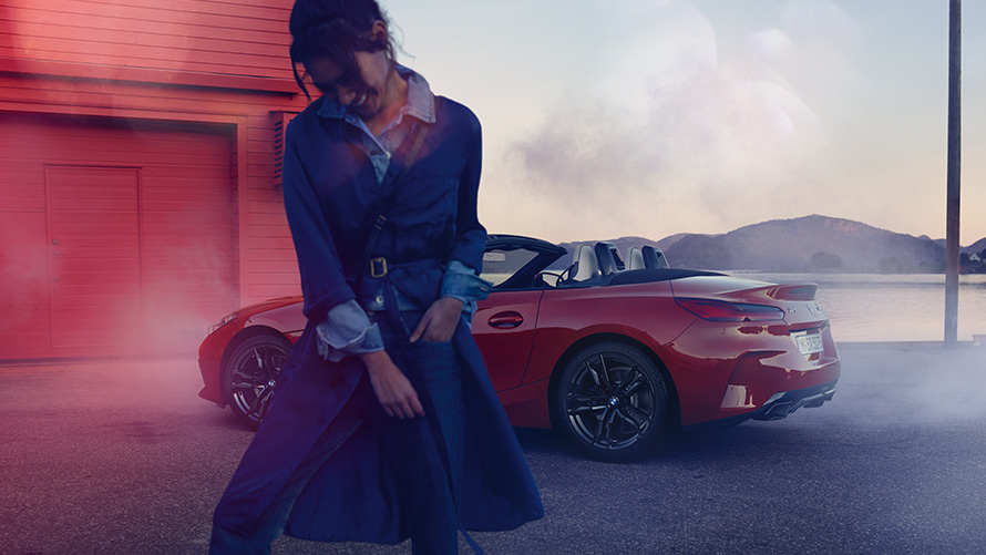 BMW Z4 M40i Roadster G29 со сложенным мягким верхом BMW Z4 M40i Roadster G29 со сложенным мягким верхом, вид сзади с поворотом в три четверти, и женщина на переднем плане