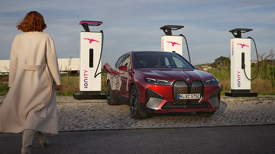 BMW Специальные программы продаж Устойчивое развитие Обзор Зарядные решения BMW Автомобиль BMW на зарядной станции и женщина на переднем плане